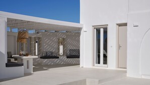 A modern outdoor pool area with a white building, a seating area with cushions, and a wicker basket. - Maestro Villas Naxos (Naxos)