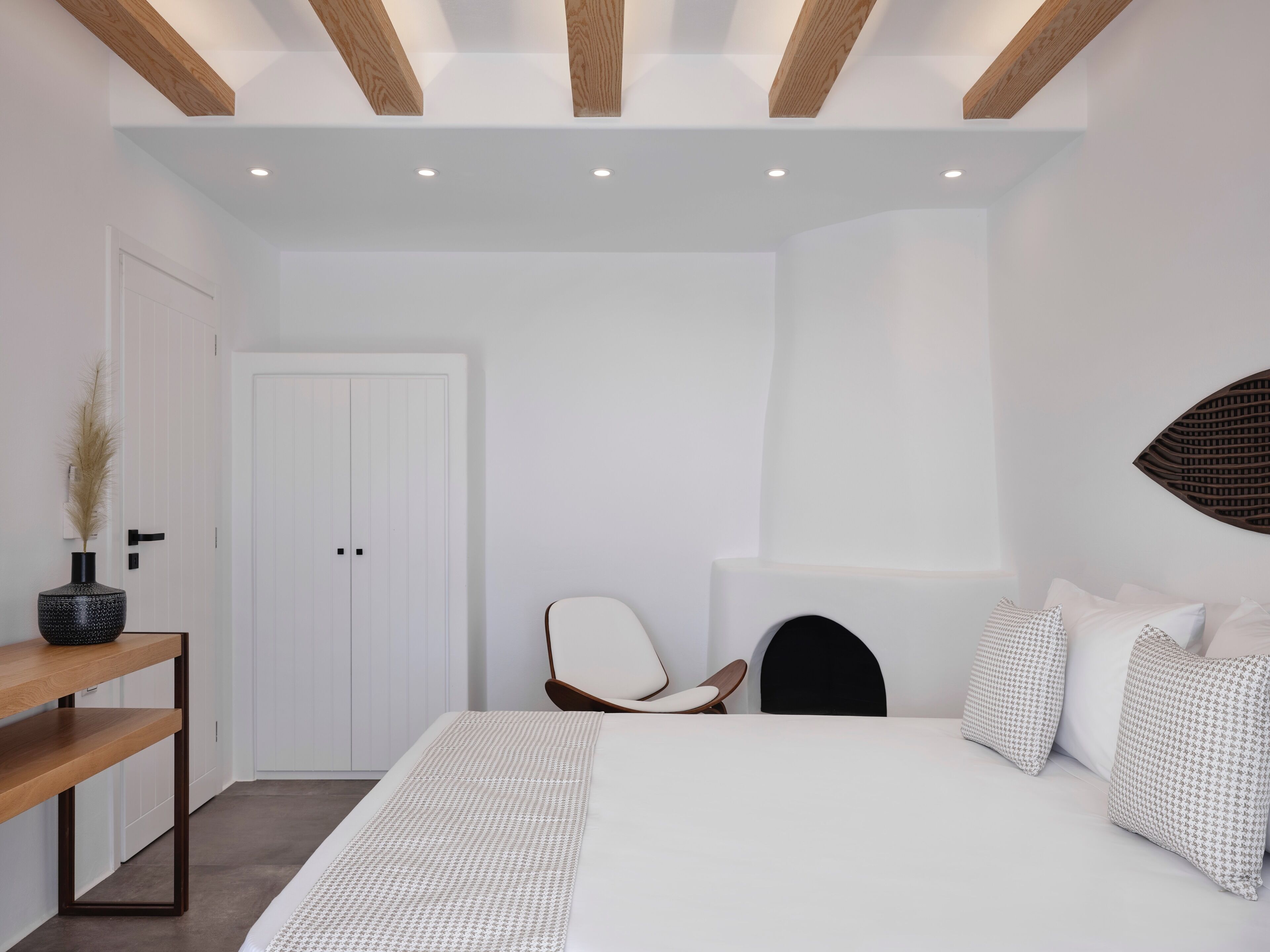 A modern bedroom with a large bed, a wooden nightstand, a chair, and a decorative wall piece.