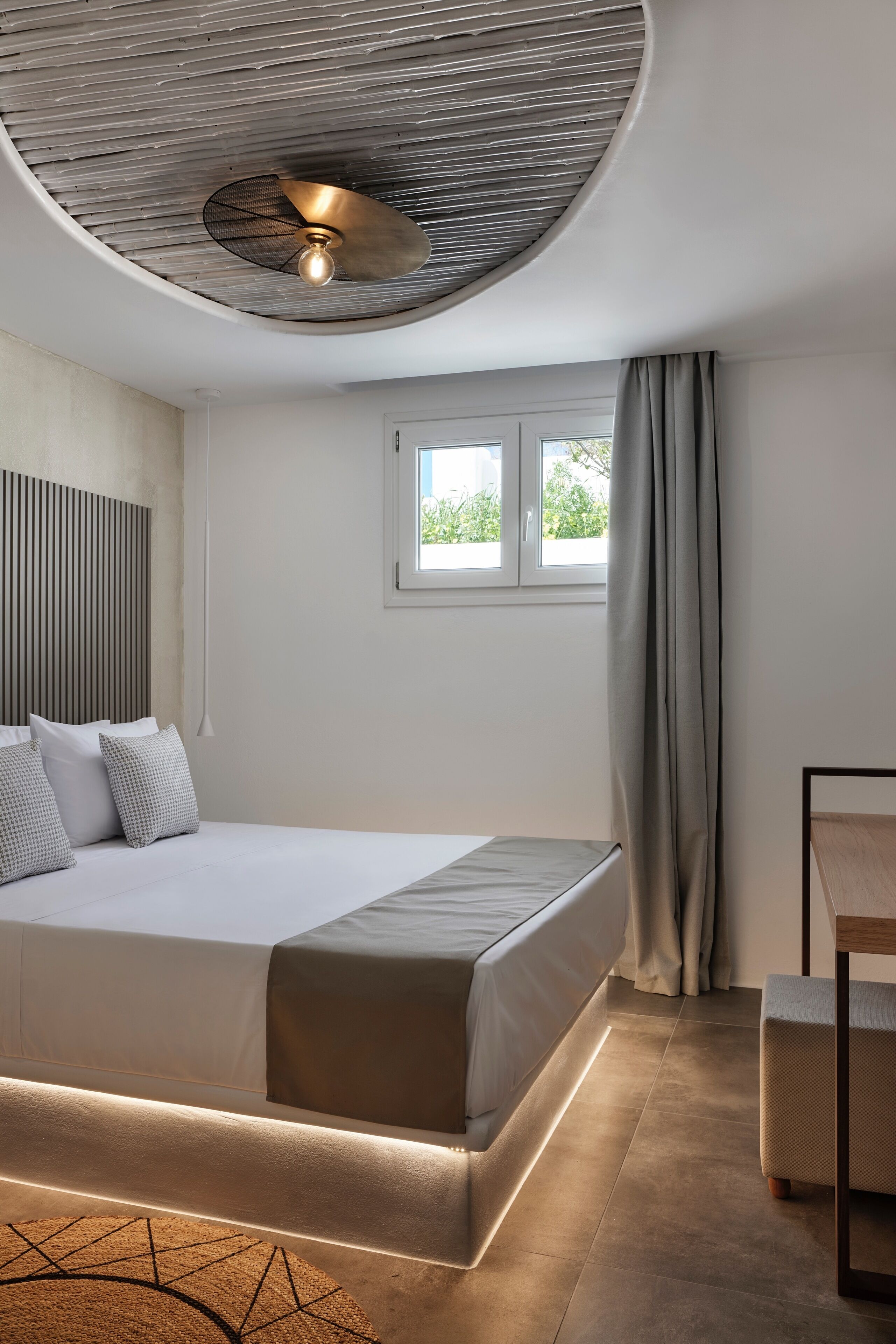Een moderne slaapkamer met een groot bed, een plafondventilator, een raam met gordijnen en een nachtkastje.