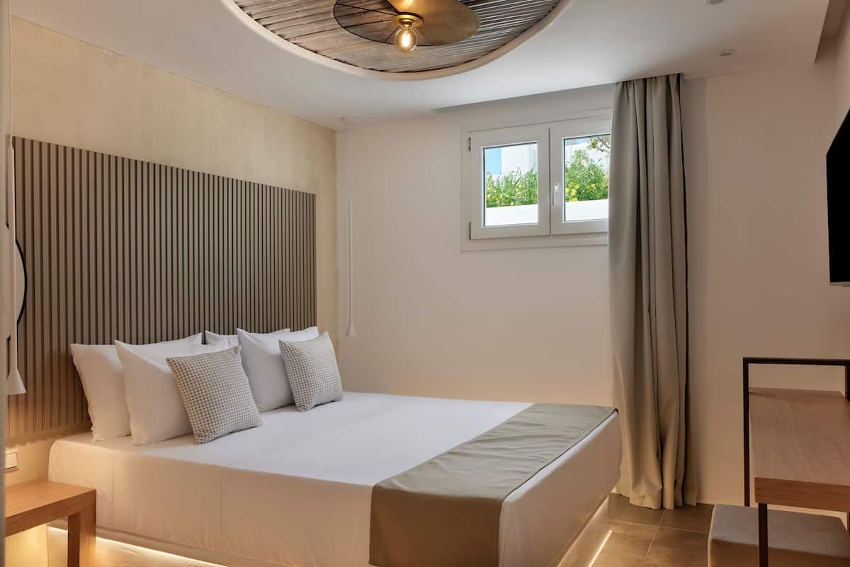 Un dormitorio moderno con una cama grande, un ventilador de techo, una ventana con cortinas y un televisor sobre un mueble.