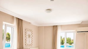 A hotel room with a large bed, a chair, a table, and a view of a swimming pool. - Amadeus Motel (Cinarcik)