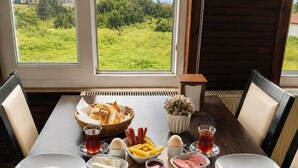 A dining table with a variety of food items and a view of the sea through large windows. - Amadeus Motel (Cinarcik)