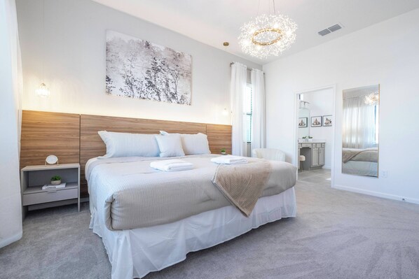 Une chambre moderne avec un grand lit, une table de chevet avec une lampe, une œuvre d’art accrochée au mur et un lustre.