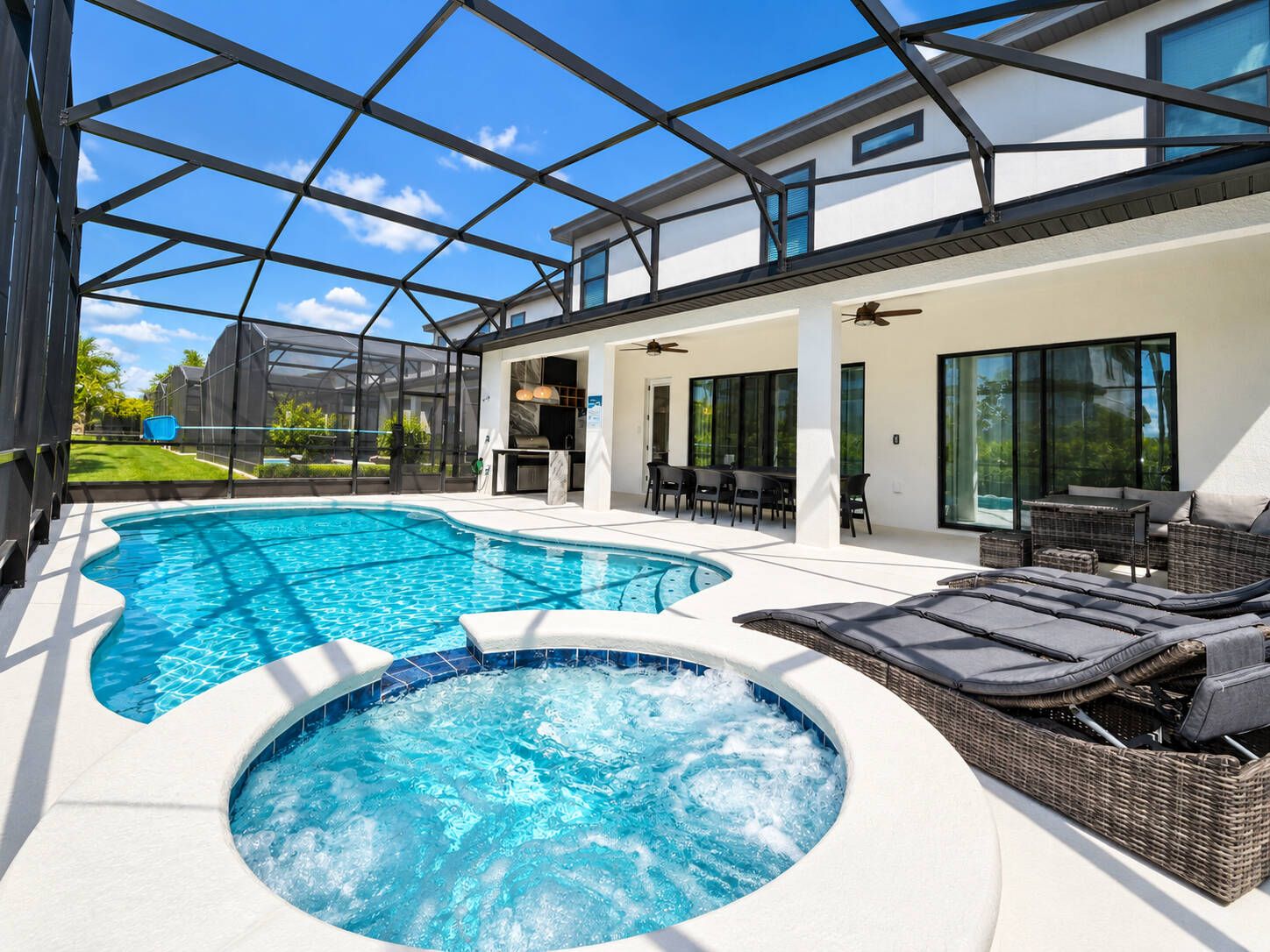 A modern outdoor pool area with a hot tub, seating, and a covered patio.