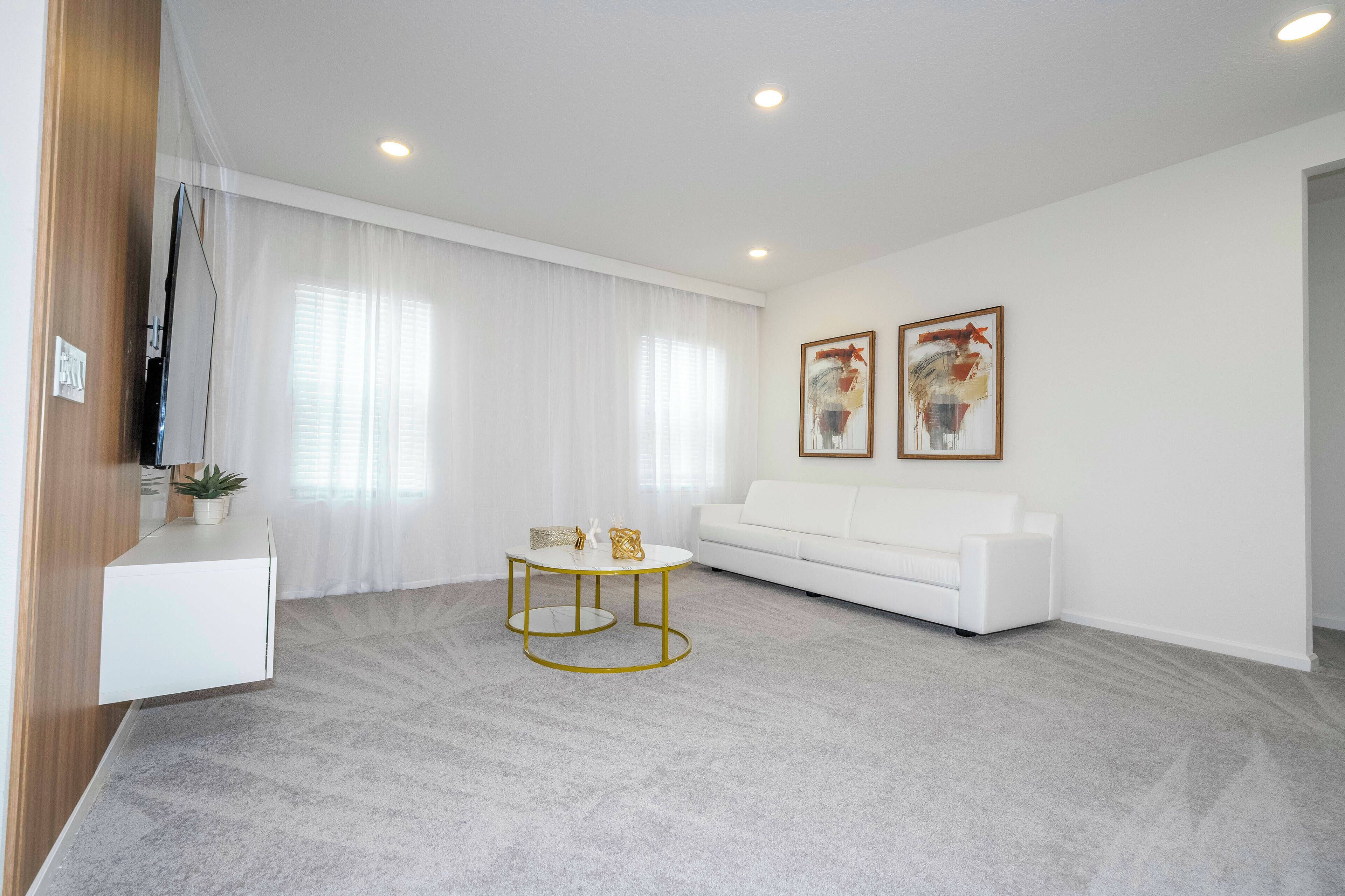 Ein modernes Wohnzimmer mit einem weißen Sofa, einem Couchtisch mit goldener Rahmung und zwei gerahmten Kunstwerken an der Wand.