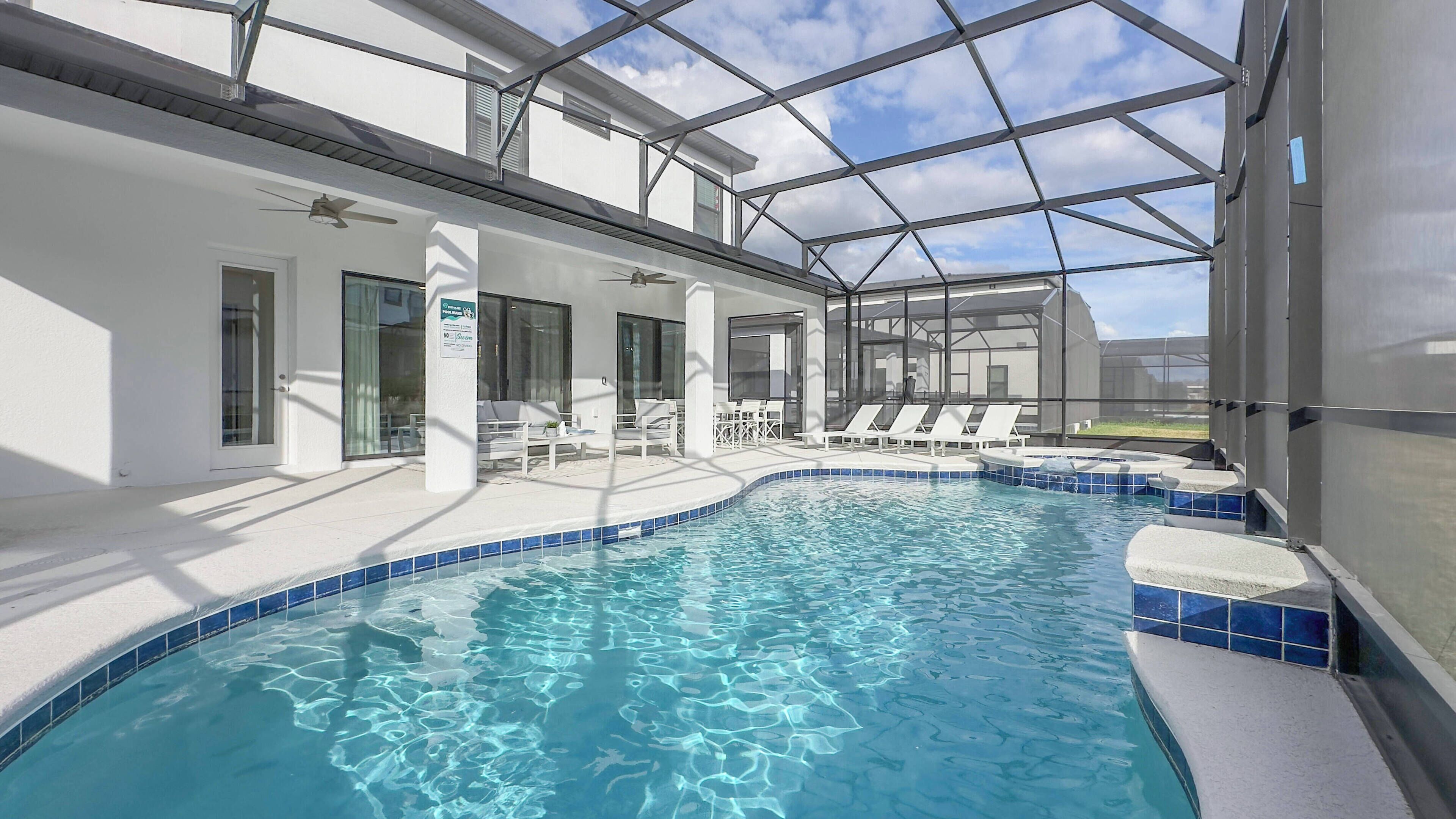A pool area with clear blue water, white lounge chairs, and a covered seating area with a glass roof.