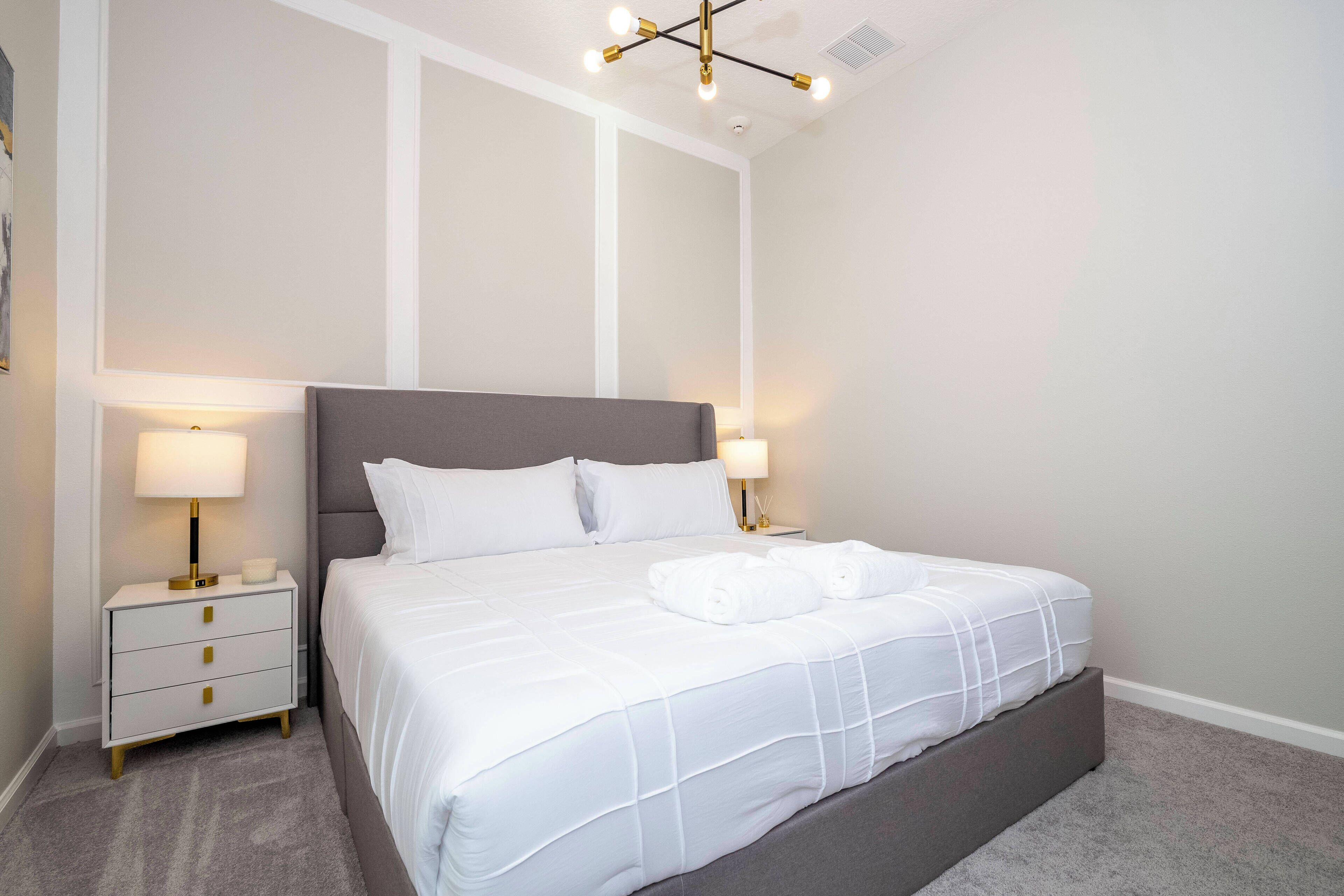 A neatly made bed with white linens and two pillows, a bedside table with a lamp, and a modern ceiling light fixture.