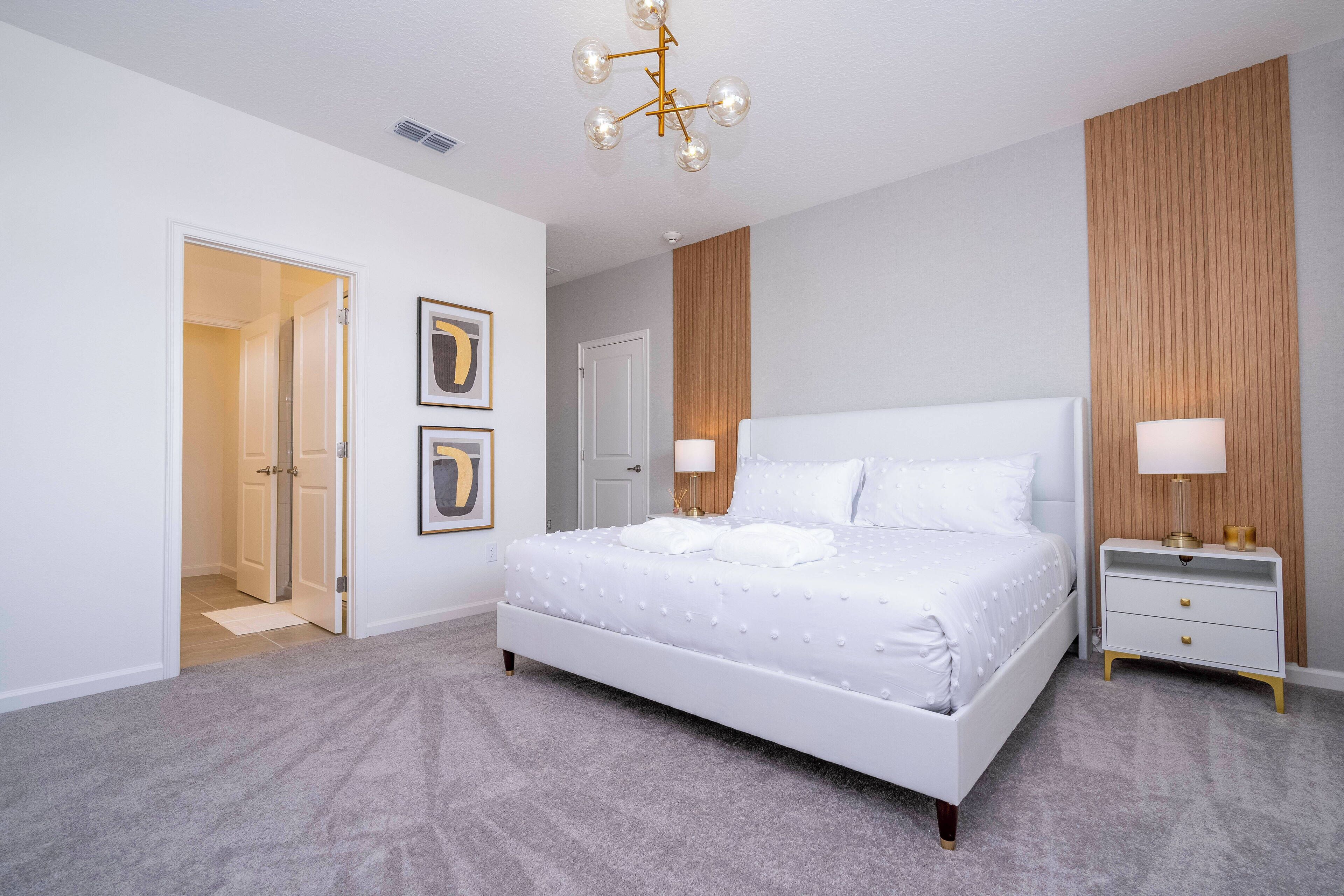 A bedroom with a large bed, bedside tables, a chandelier, and framed artwork on the wall.