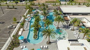 Eine Vogelperspektive eines Hotels mit einem großen Swimmingpool, umgeben von Palmen und Liegestühlen.
