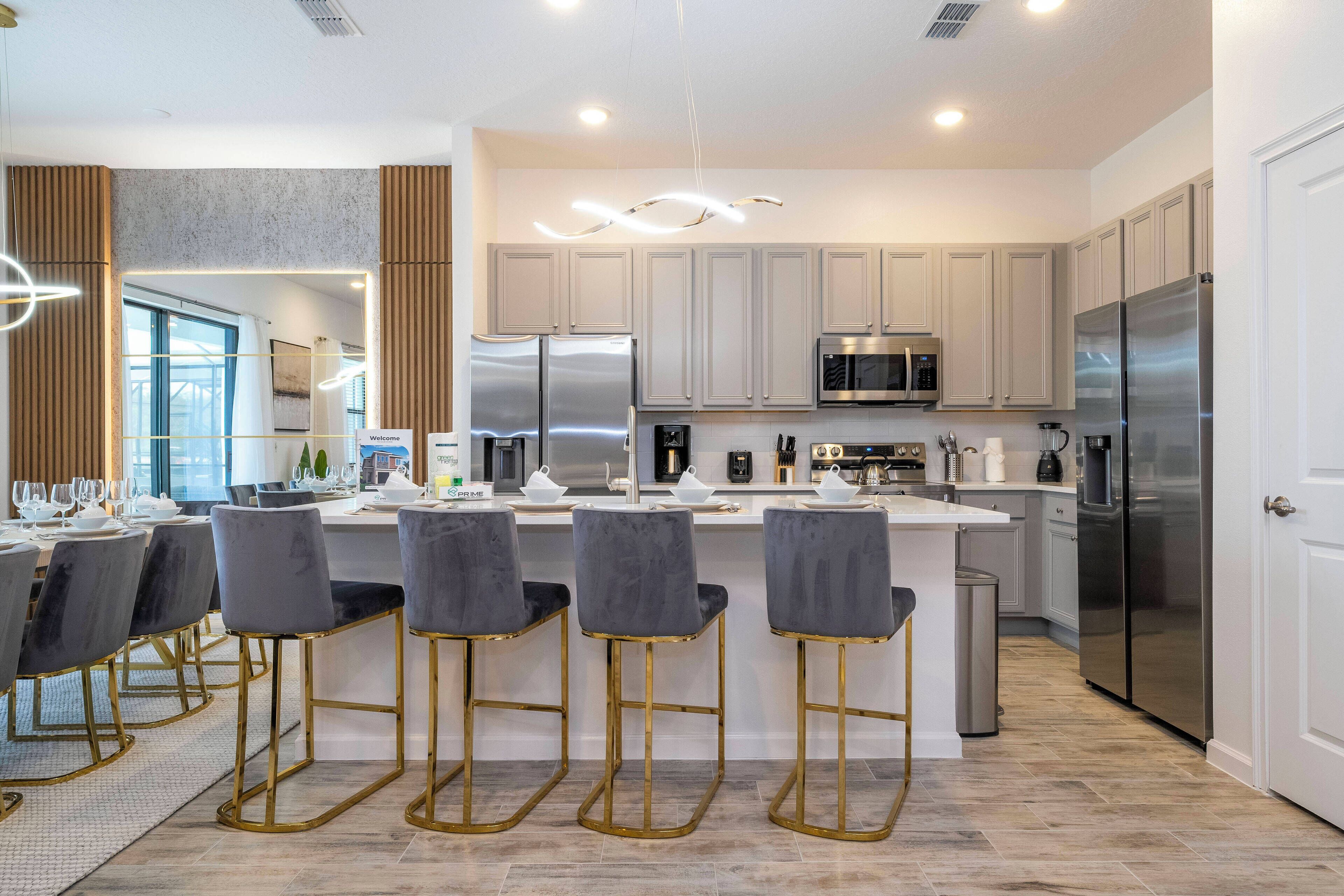 A modern kitchen with a central island, bar stools, stainless steel appliances, and a view to the dining area.