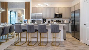 A modern kitchen with a central island, bar stools, stainless steel appliances, and a view to the dining area. - The Best Home and Location Near Disney (6139PG) (Orlando)