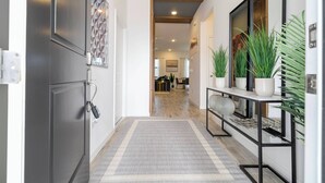 A hallway with a modern design, featuring a grey rug, a console table with potted plants, and a door with a key lock. - The Best Home and Location Near Disney (6139PG) (Orlando)