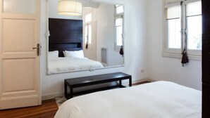 A bedroom with a large bed, a bench, a mirror, and a hanging light fixture. - Purple Rain Elegant 2 Bedroom in Recoleta (Buenos Aires)
