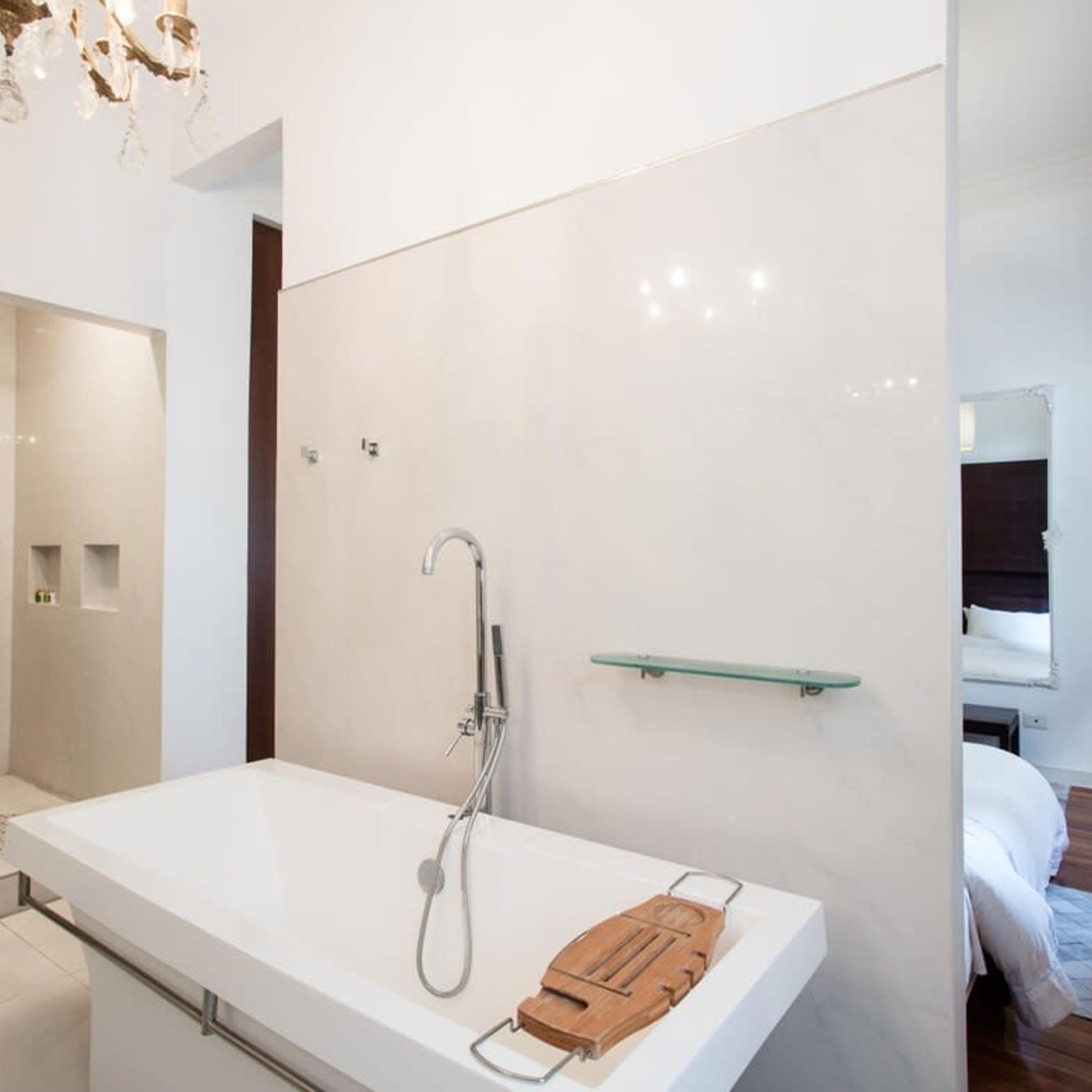 Ein modernes Badezimmer mit einem weißen Waschtisch, einer Dusche inklusive Handbrause und einer Holz-Badezimmermatte auf dem Boden.