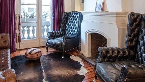 A living room with a fireplace, leather armchairs, a sofa, and a cowhide rug. - Purple Rain Elegant 2 Bedroom in Recoleta (Buenos Aires)