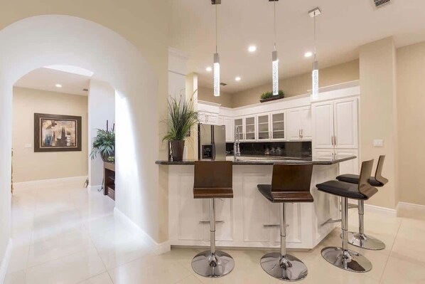 A modern kitchen with three bar stools, white cabinetry, and pendant lighting.