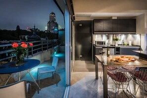 A modern kitchen with dark cabinets, a dining area with a table and chairs, and a view of a cityscape at dusk.