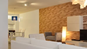 A modern living room with a white sofa, a wooden accent wall, and a television. - Green Bliss Spacious Studio in Nu ez (Buenos Aires)