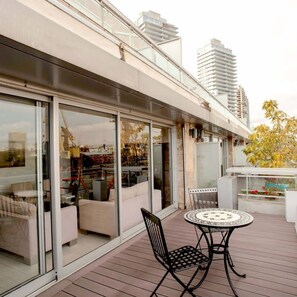 Enjoy a balcony with a sofa, coffee table, and single chair, offering a view of the surrounding high-rise buildings and lush greenery.