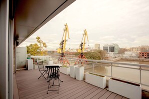 A balcony with a table and chairs, overlooking a river with construction cranes in the background. - Dique Madero Amazing 2 Bedroom in Puerto Madero (Buenos Aires)