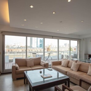 Relax in this spacious living room with a large glass coffee table and two sofas, offering a comfortable seating area with a view of the city.