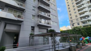 Un moderno edificio de gran altura con varios balcones, entrada vigilada y un área de juegos con equipos de colores.