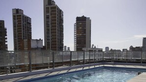 Une piscine sur le toit, avec une eau d’un bleu cristallin, entourée d’une clôture métallique et avec les bâtiments de la ville en arrière-plan.