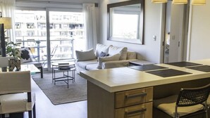 Une cuisine moderne dotée d’un îlot central, un coin repas avec une table et des chaises, et un espace de vie avec un canapé et une grande fenêtre.