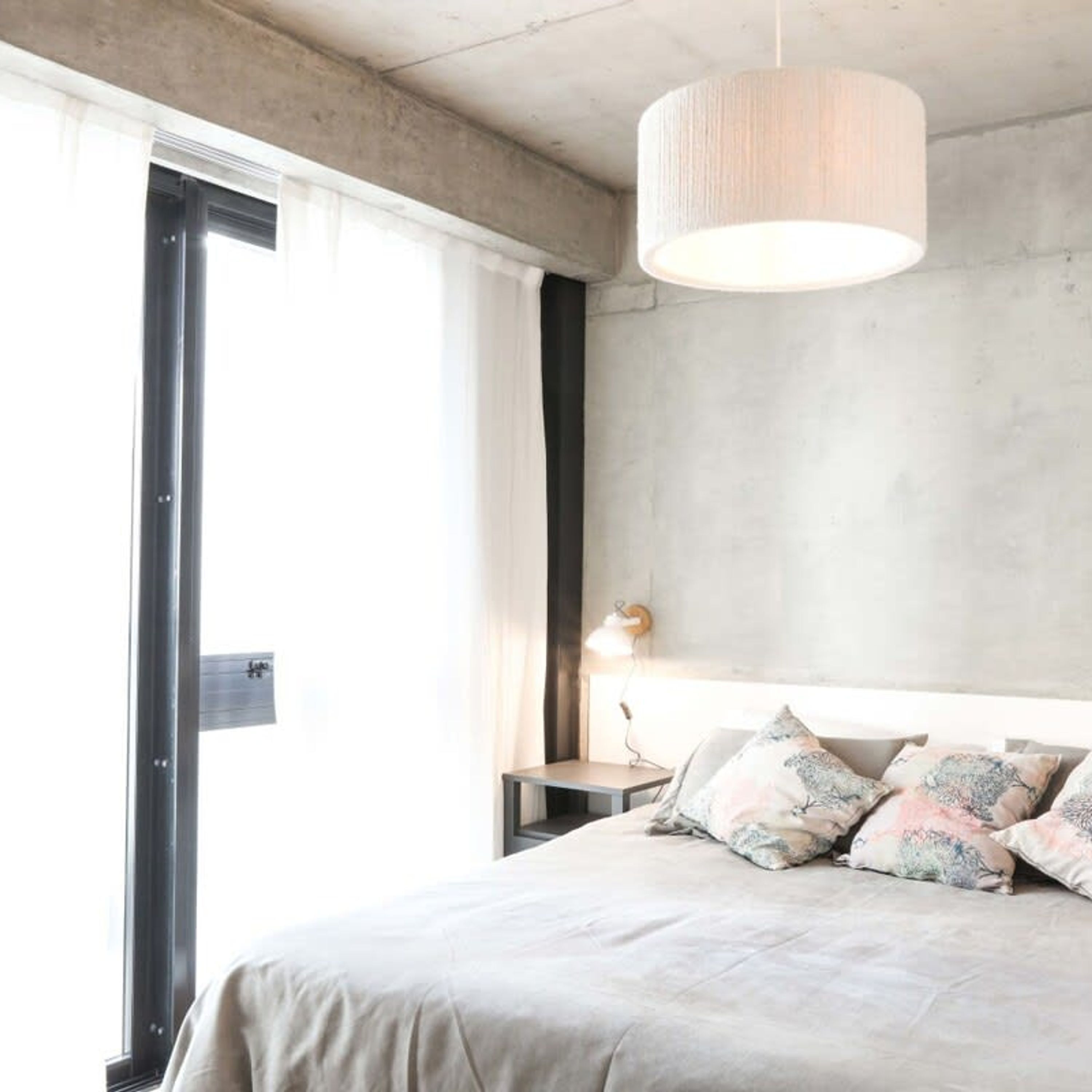 A modern bedroom with a large bed, a bedside table with a lamp, and a view of the outdoors through a large window.