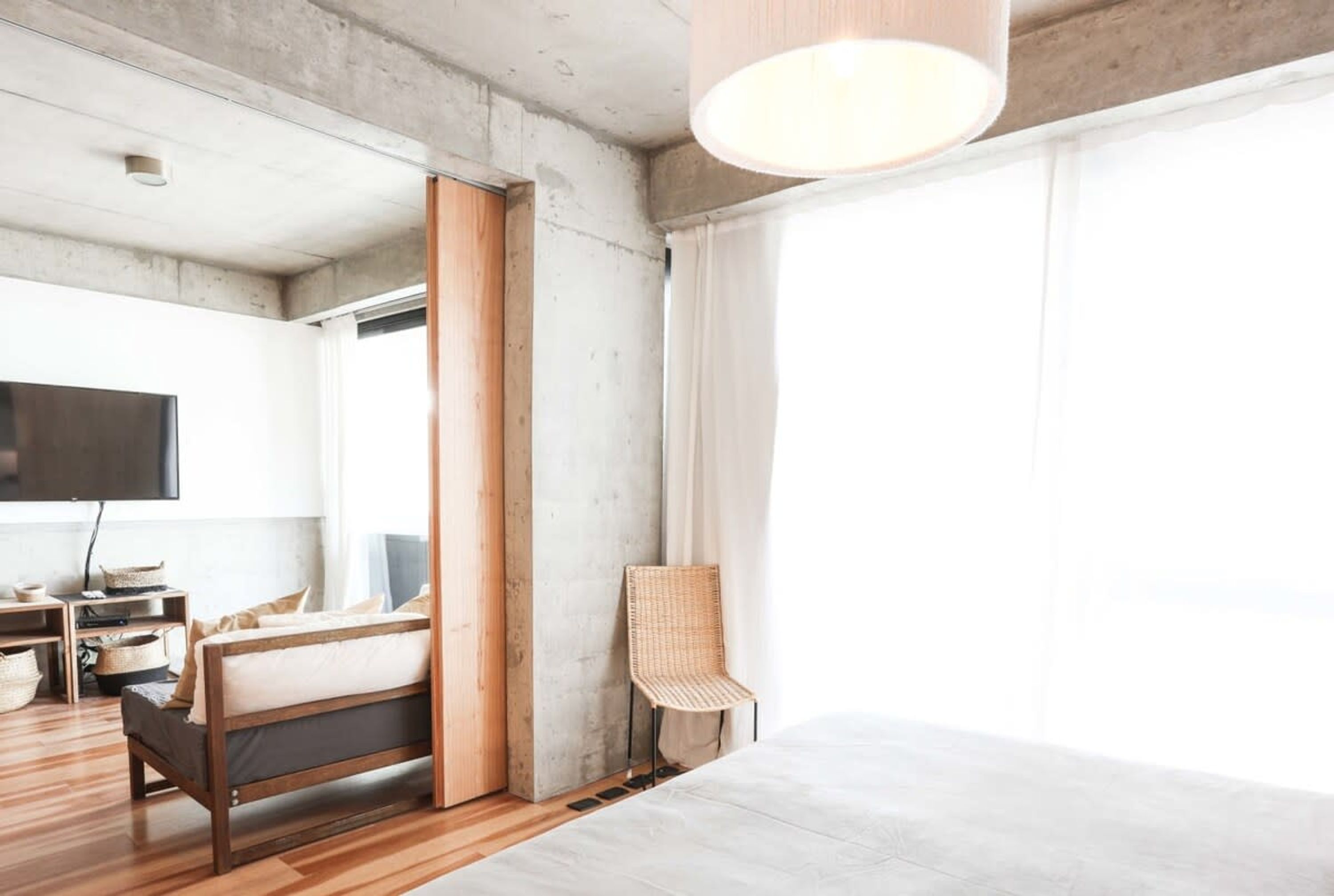 Quarto moderno com cama de madeira, uma cadeira de vime e uma janela grande.