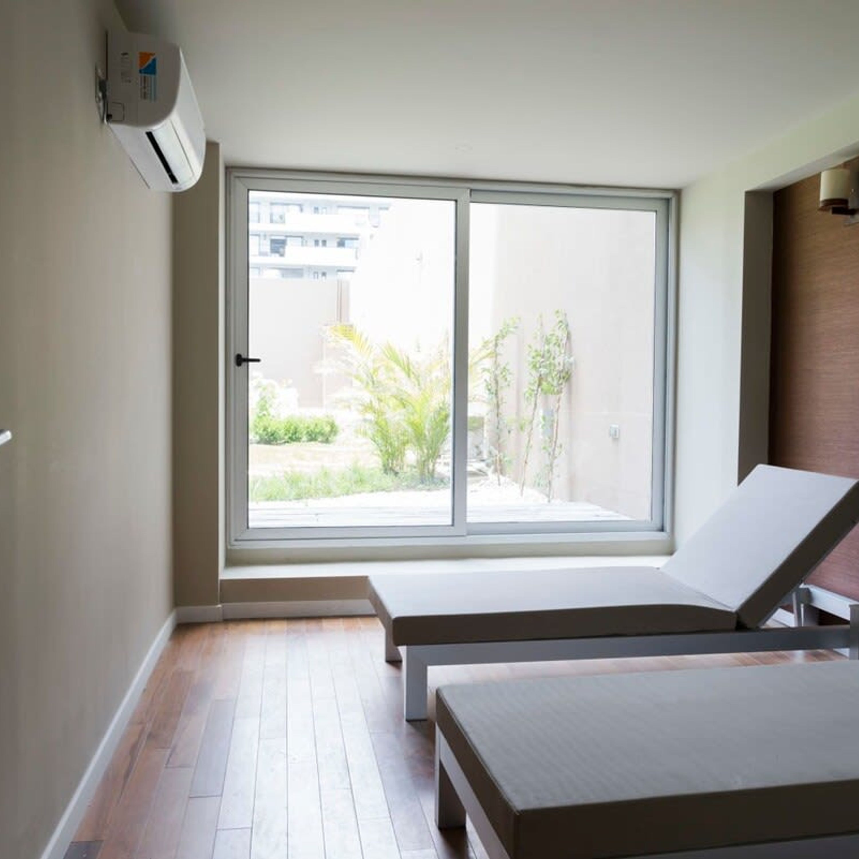 Une chambre d’hôtel dotée d’une grande porte-fenêtre coulissante donnant sur l’extérieur, d’un plancher en bois et de deux fauteuils de détente blancs.