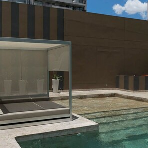 Area piscina moderna all'aperto con zona relax chiusa in vetro, un piccolo elemento d'acqua e piante in vaso.