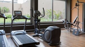 Ein Fitnessstudio mit Laufbändern, Crosstrainern und Fahrrädern, große Fenster mit Blick auf Grünflächen und Holzböden.