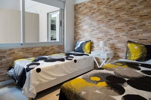 Un dormitorio con dos camas, una mesita de noche blanca, una lámpara blanca y una pared con diseño de ladrillo.