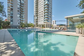 A swimming pool with lounge chairs, surrounded by tall residential buildings.