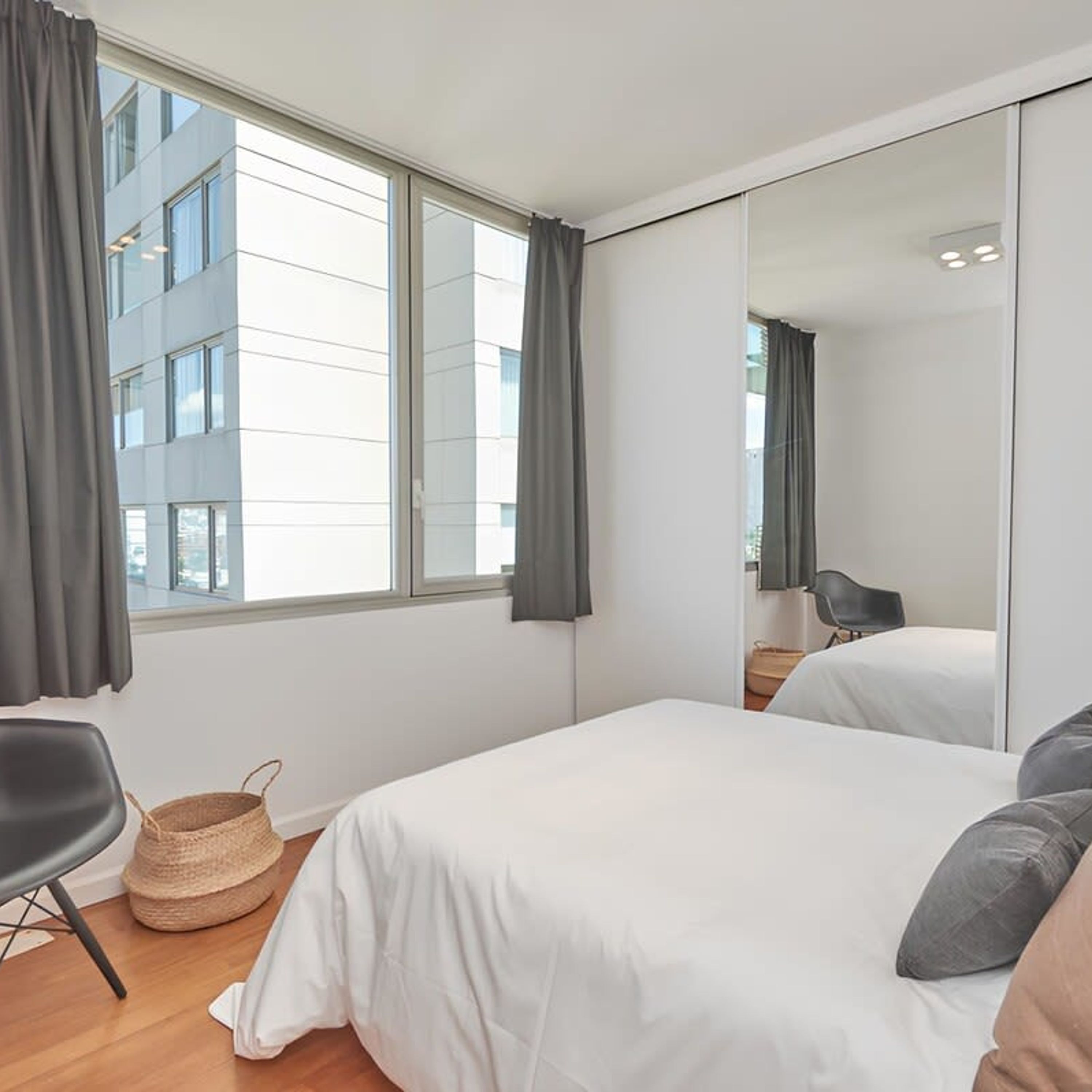 Un dormitorio moderno con una ventana grande, una cama, una silla y un espejo.