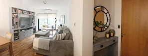 En stue med sofa, fjernsyn, bogreol og en dør med et rundt spejl.