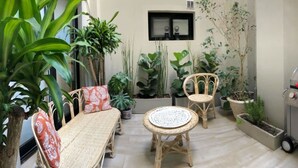Eine Terrasse mit Korbmöbeln, Blumentöpfen und einem Grill.