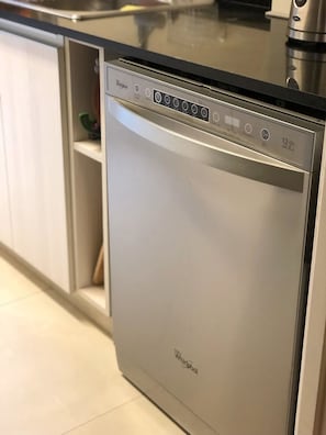 En Whirlpool opvaskemaskine med kontrolpanel, placeret i et køkken med hvide skabe og et rustfrit stål emfang.