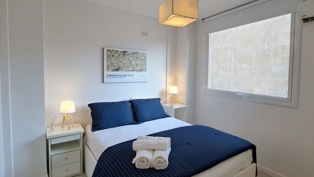 A modern bedroom with a large bed, two bedside tables with lamps, a window, and a ceiling light fixture. - Alto Guemes I Spacious 1BR in Palermo (Buenos Aires)