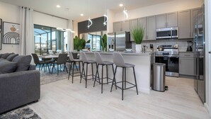 A modern kitchen with stainless steel appliances, a bar area with stools, and a dining area with a pool view. - 8BR Made for Families, Built for Fun (5878PG) (Orlando)