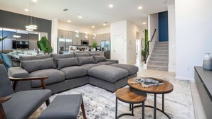 A modern living room with a sectional sofa, a coffee table, and a dining area with a table and chairs. - 8BR Made for Families, Built for Fun (5878PG) (Orlando)