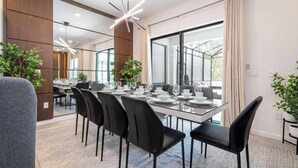 A modern dining area with a long table set for six, surrounded by black chairs, and a large window with curtains.