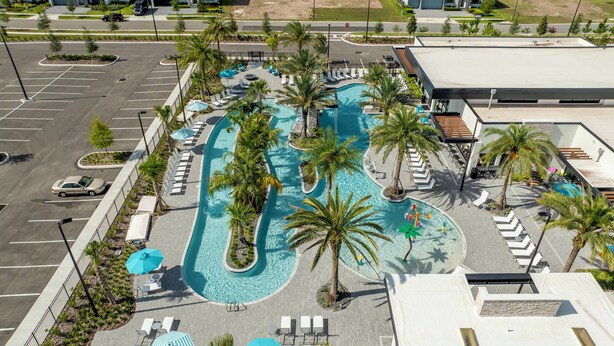 An aerial view of a hotel with a large swimming pool surrounded by palm trees and lounge chairs.