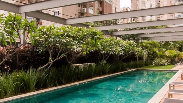 A swimming pool with a tiled edge, surrounded by greenery and a wooden deck with lounge chairs. - Vila Nova Amazing 1-bedroom in Vila Nova Concei o (São Paulo)