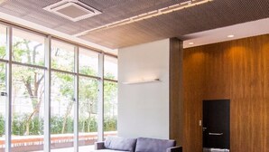 A spacious lobby with a modern sofa, a coffee table, and large windows offering a view of greenery outside. - Vila Nova Amazing 1-bedroom in Vila Nova Concei o (São Paulo)