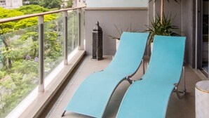 A balcony with two blue lounge chairs, a potted plant, and a projector screen. - Vila Nova Amazing 1-bedroom in Vila Nova Concei o (São Paulo)