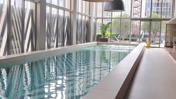 Une piscine intérieure moderne, dotée de grandes fenêtres et de luminaires suspendus noirs.