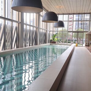 A modern indoor swimming pool with large windows and black pendant lights. - Pinheiros Silver I Modern Studio in Faria Lima (São Paulo)