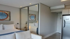 Une chambre d’hôtel moderne avec un grand lit, un canapé blanc, un miroir et un réfrigérateur.